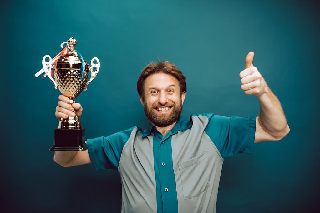Man smiling, showing a thumbs up sign, and holding a trophy.