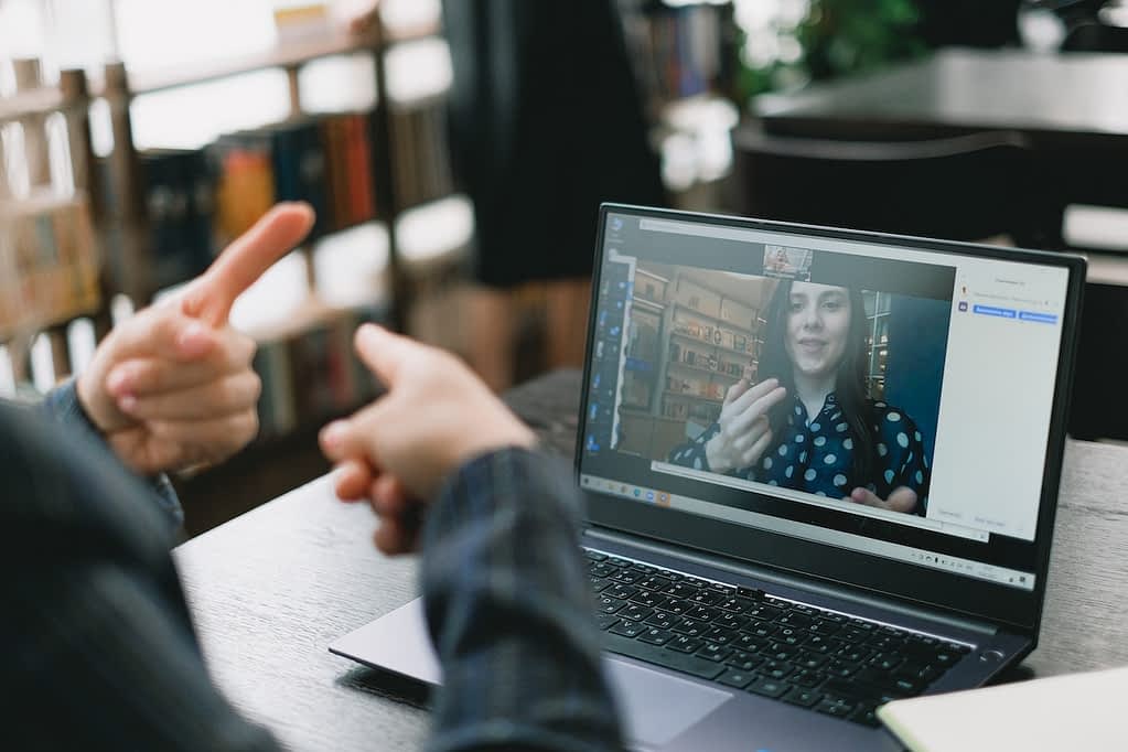 Man engaged with video chat with girl on laptop and using sign language.