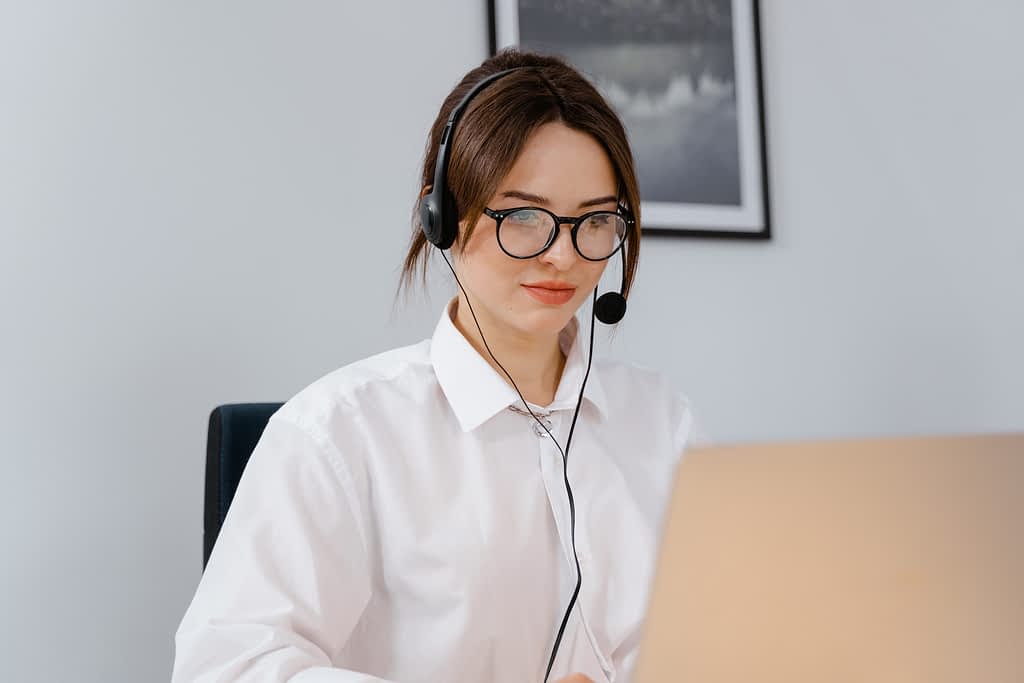Female virtual receptionist wearing a headset and looking at a laptop.